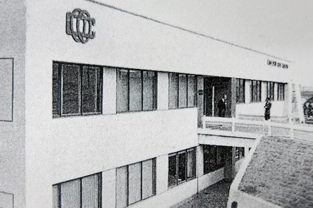 新幹線の通信・信号機器室として使われた、モダンなデザインの白い二階建ての建物。入口上部には企業ロゴが見え、職員らしき人物が立っている写真。